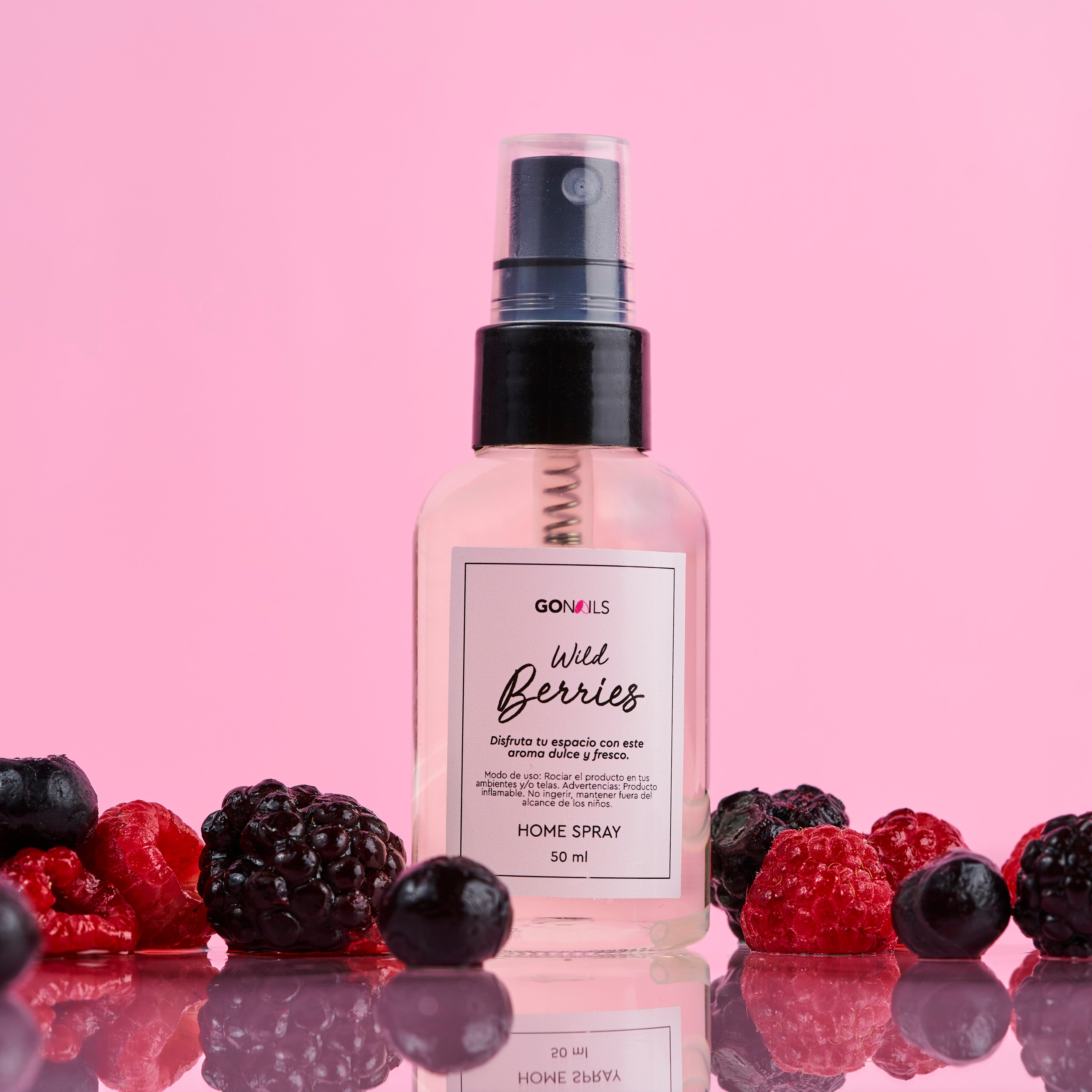 Home Spray Wild Berries en frasco con frutas rojas sobre fondo rosa